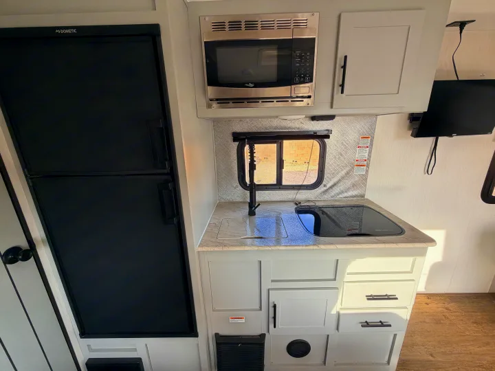 Modern rv rental kitchenette featuring a black Dometic fridge, stainless microwave, sink, and glass cooktop. Compact and efficient.. Forest River Vibe 2021