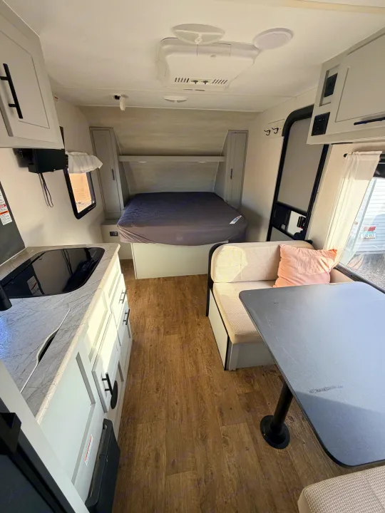 Interior of an RV rental featuring a comfortable bed, dinette with table, and a functional kitchenette area.. Forest River Vibe 2021