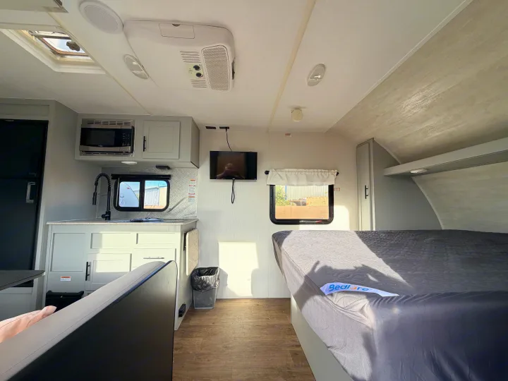 Bright RV rental interior featuring a kitchen (microwave, sink), bed, ceiling AC, TV, skylight, and dinette.. Forest River Vibe 2021