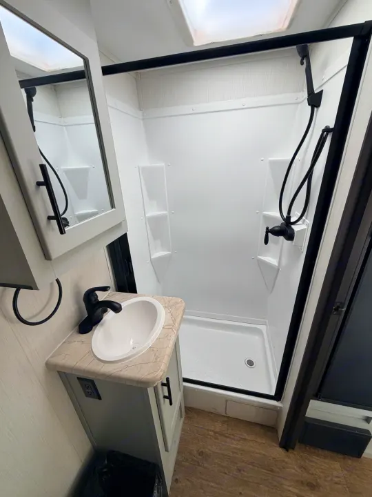 RV rental bathroom: A bright, compact space featuring a modern shower with black trim, vanity, sink, and mirrored cabinet.. Forest River Vibe 2021
