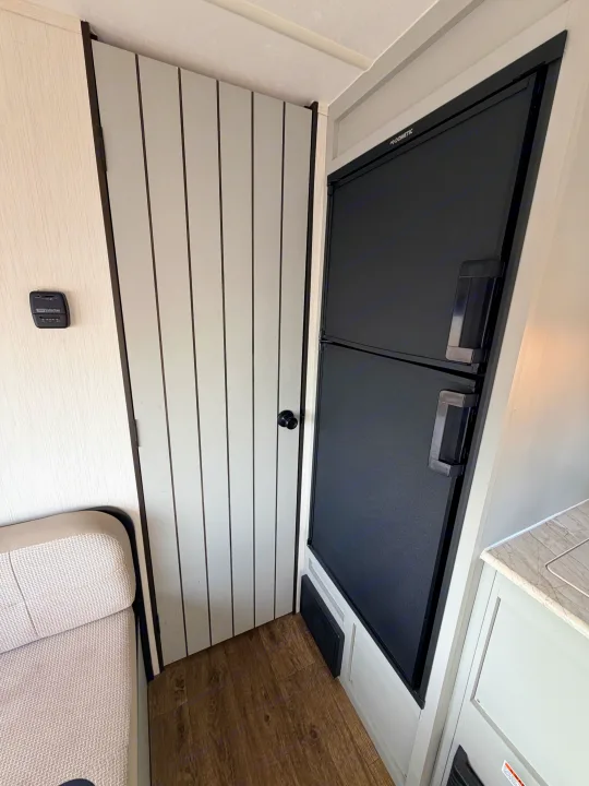 RV rental: Compact interior with a black Dometic fridge, a white vertical-striped door, and a Suburban thermostat.. Forest River Vibe 2021