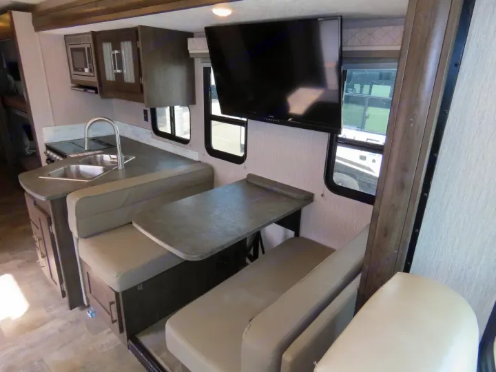 RV rental interior featuring a kitchen with sink, microwave, dinette with table & benches, TV, and bunk beds.. Coachmen PURSUIT 31BH 2023