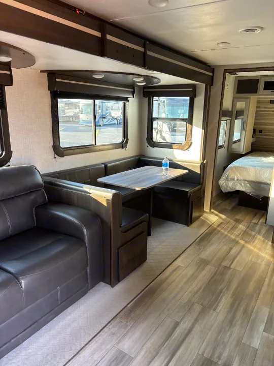Modern RV rental interior: large sofa, U-shaped dinette with table, and visible bedroom. Wood-look and patterned flooring.. Crossroads RV Cruiser Aire 2022