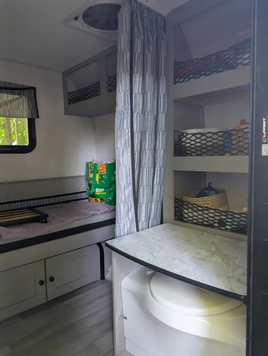 View inside a compact **rv rental** showing a toilet, shower, bed, window, and netted storage shelves.. Coachmen Viking 1200ROK 2025
