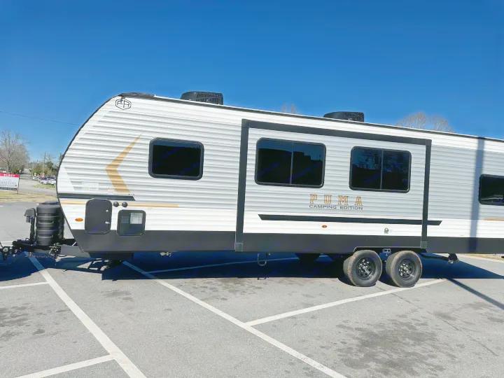 A sleek Puma Camping Edition travel trailer, ready for an RV rental adventure, parked in an asphalt lot under a blue sky.. Forest River Palomino Puma Camping Edition 2025