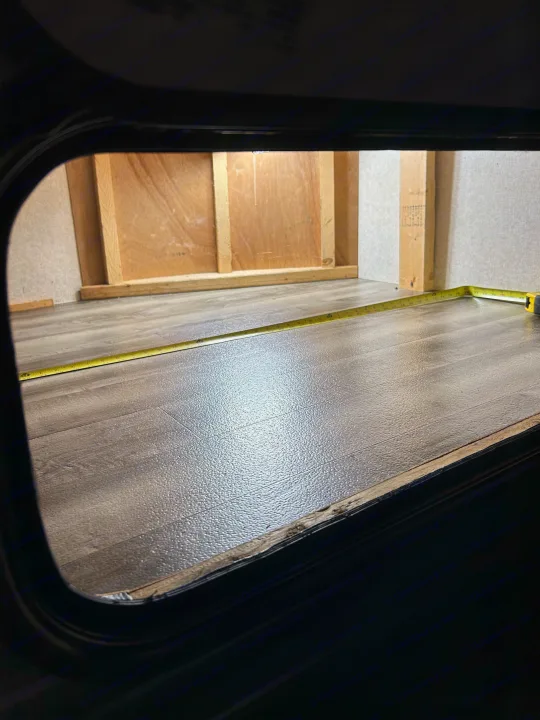 RV rental storage compartment being measured with a tape measure, showing wood framing and new textured flooring.. Jayco Jay Flight SLX 2018