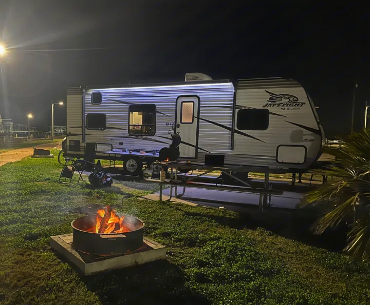 Night scene: RV rental illuminated by streetlights and a cozy campfire. A gravel path leads to distant buildings.. Jayco Jay Flight SLX 2018