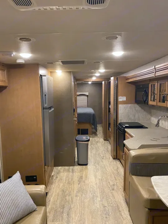 Inside an RV rental, showing a well-equipped kitchen, dining booth, refrigerator, and a hallway leading to a bedroom.. Thor Hurricane 2017