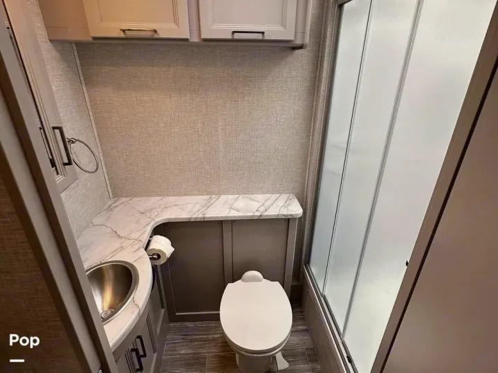 Clean RV rental bathroom featuring a toilet, stainless sink with marble-look counter, and frosted glass shower.. Thor Hurricane 2017