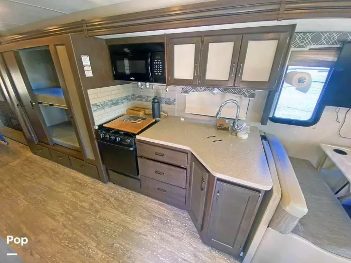 This RV rental features a compact kitchen with a microwave, stove, sink, and adjacent bunk beds and a dinette.. Thor Hurricane 2017
