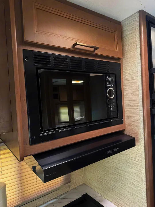 Modern Greystone microwave and integrated range hood in an RV rental kitchen, surrounded by light wood cabinetry.. Thor Coleman 2023