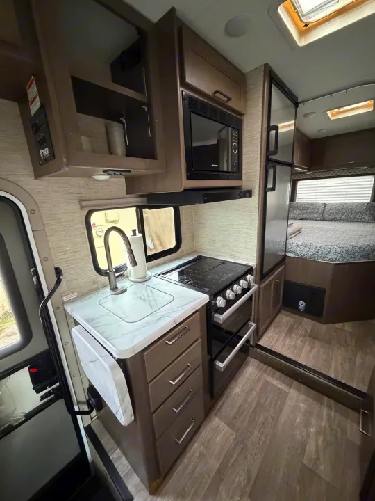 Compact rv rental interior featuring kitchen with stove, microwave, fridge, and cozy bedroom.. Thor Coleman 2023