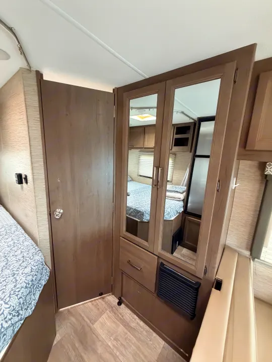 This RV rental showcases a cozy bedroom setup with a patterned bed, mirrored wardrobe, and convenient storage solutions.. Thor Coleman 2023