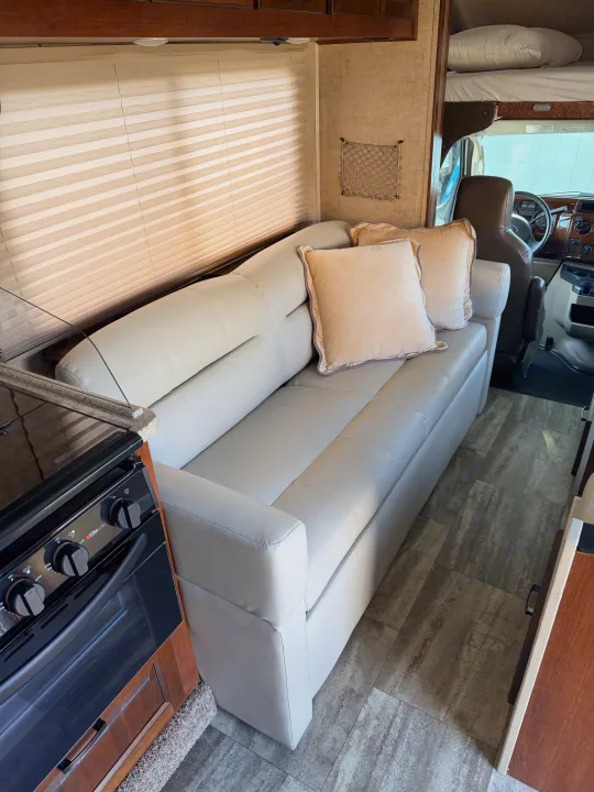Modern RV rental interior: light sofa, kitchen stove, window blinds, overhead bunk bed, and driver's cockpit. Clean design.. Forest River Forester 2861DS 2016