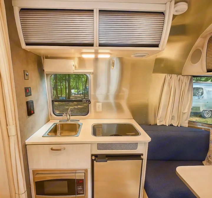 Step inside this RV rental's sleek kitchen and dinette, featuring a sink, stovetop, microwave, and fridge, all within a compact layout.. Airstream Bambi 2024
