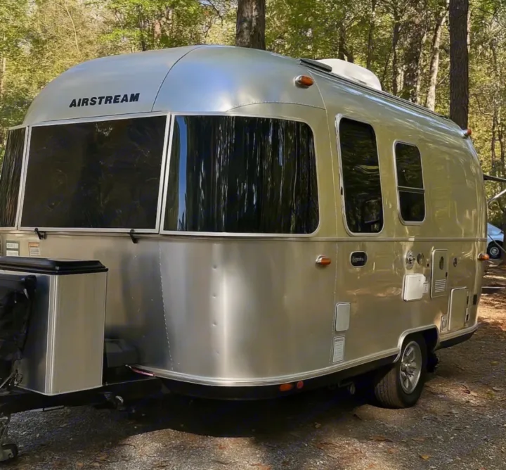 This shiny Airstream RV rental is perfect for a cozy camping adventure, nestled among tall trees in the outdoors.. Airstream Bambi 2024