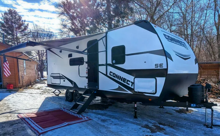 White and black travel trailer RV rental parked on snow with an awning out, ready for winter camping.. KZ Connect SE 2025