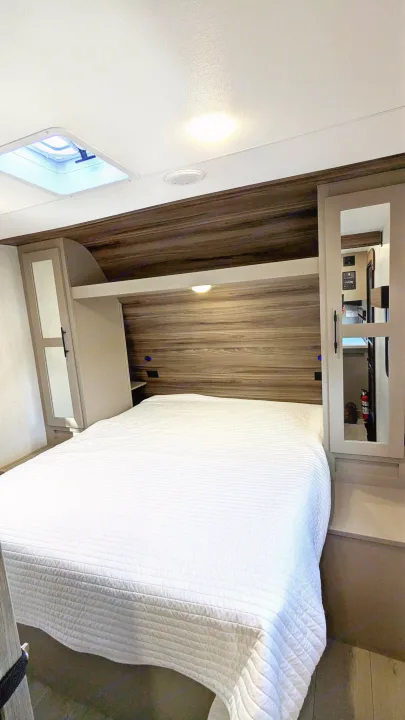 Rv rental bedroom: a comfy white-quilted bed, wooden headboard, overhead cabinets, and a skylight for natural light.. KZ Connect SE 2025