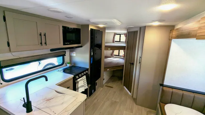 This modern RV rental features a well-equipped kitchen with a stylish faucet, a cozy dining area, and convenient bunk beds.. KZ Connect SE 2025