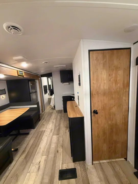 Spacious RV rental interior features a dinette, wood-look flooring, modern cabinetry, and private bedroom access.. Keystone RV Springdale 2022