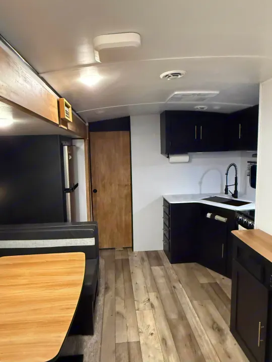 Modern RV rental interior featuring a black kitchen with white countertops, a dinette, and wood-look flooring.. Keystone RV Springdale 2022