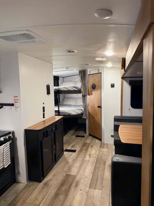 Spacious RV rental interior with kitchen, black cabinets, dinette, and bunk beds visible. Light wood-look flooring throughout.. Keystone RV Springdale 2022