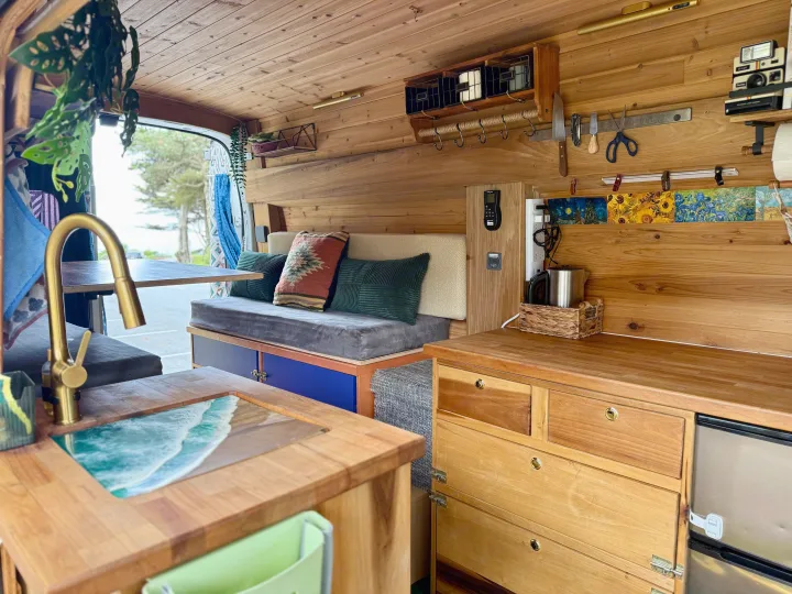 Cozy wood-paneled rv rental interior. Features kitchen with ocean-themed sink, comfortable seating, and custom storage for van life.. Ford Transit 2019
