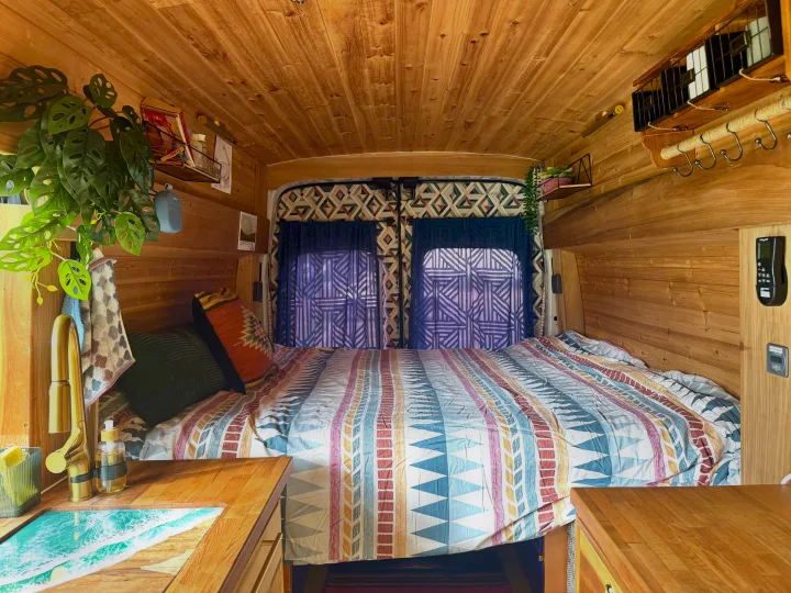 Warm wood-paneled RV rental interior: a cozy bed, unique ocean-themed sink, and vibrant decor for a comfortable journey.. Ford Transit 2019