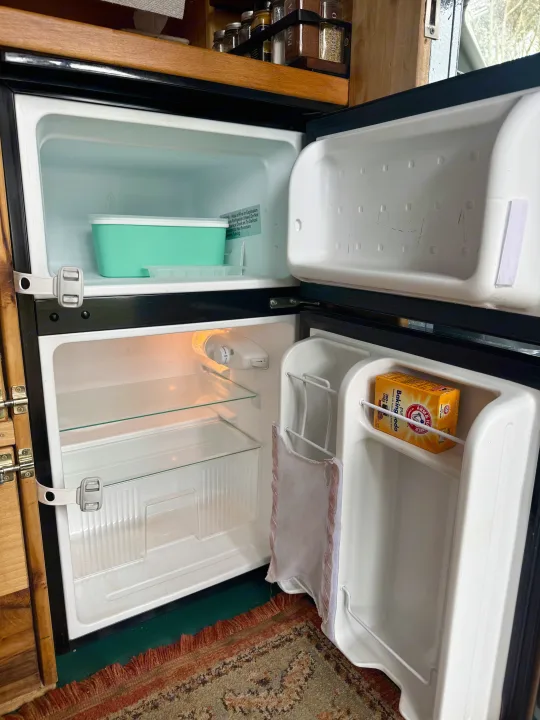 Inside an rv rental: open small refrigerator and freezer, showing baking soda on the door and latches for travel.. Ford Transit 2019