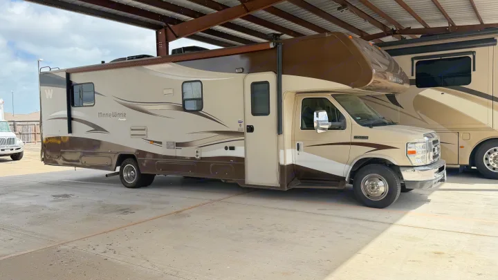 A cream and brown Winnebago Minnie Winnie Premier Class C rv rental, a motorhome, parked under a metal roof structure.. Winnebago Minnie Winnie 2015