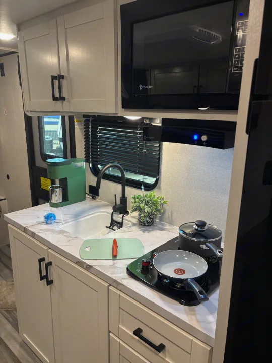 Well-equipped RV rental kitchen featuring light cabinetry, microwave, sink, coffee maker, induction cooktop, and marble-look counters.. Jayco Jay Flight SLX 2026