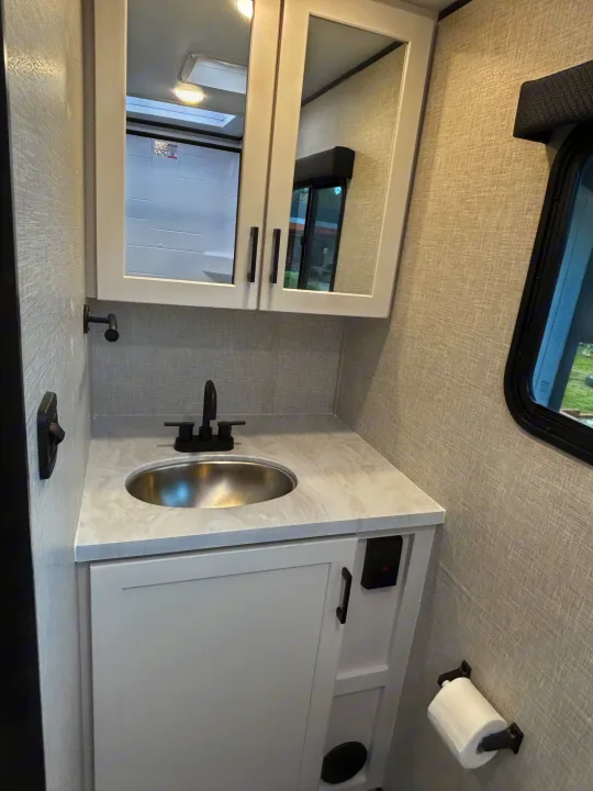 Compact RV rental bathroom with a vanity, stainless steel sink, mirror, and toilet paper holder.. Jayco Jay Feather Air 2025