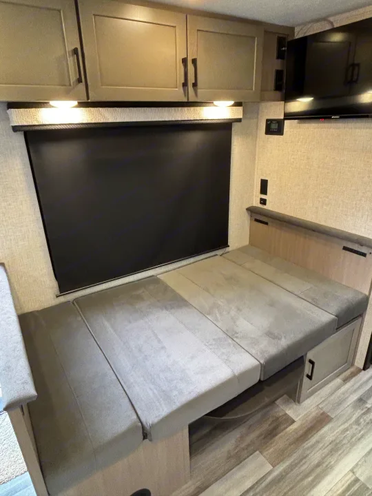 Modern RV rental interior with dinette converted to a bed, overhead cabinets, TV, and black-out blind for comfort.. Jayco Jay Feather Air 2025