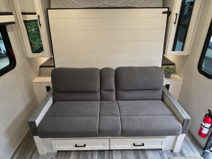 RV rental: Gray sofa with under-seat storage, a convertible wall bed, side cabinets, and a fire extinguisher.. Jayco Jay Feather Air 2025