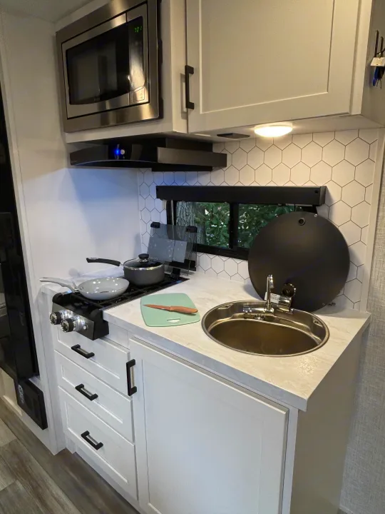 This RV rental offers a compact, modern kitchen with microwave, stovetop, sink, white cabinetry, and hexagon backsplash.. Jayco Jay Feather Air 2025