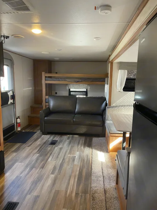 Modern RV rental living space featuring a dark sofa, bunk beds, dinette, and wood-look flooring. Includes safety amenities.. Avenger Avenger Trailer 2022