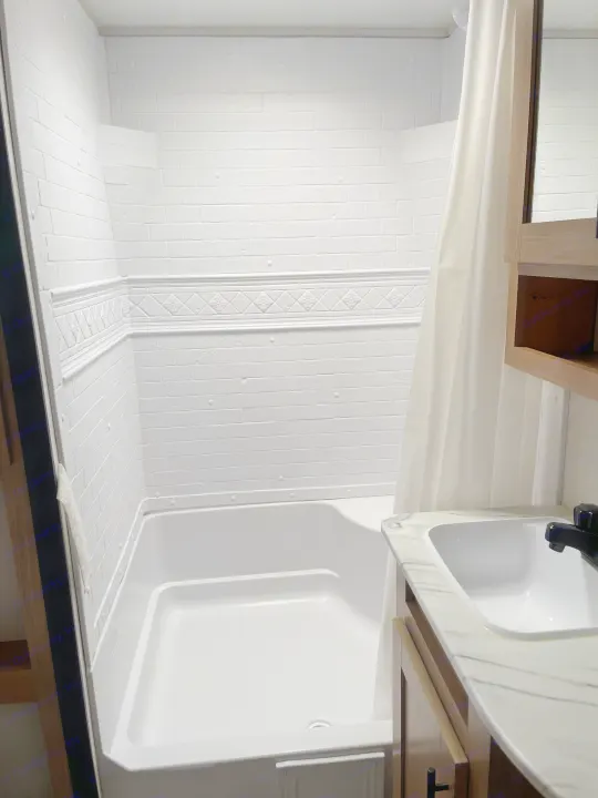 RV rental bathroom: white shower, tub, and vanity sink, with faux brick walls and a marble-look counter.. Avenger Avenger Trailer 2022