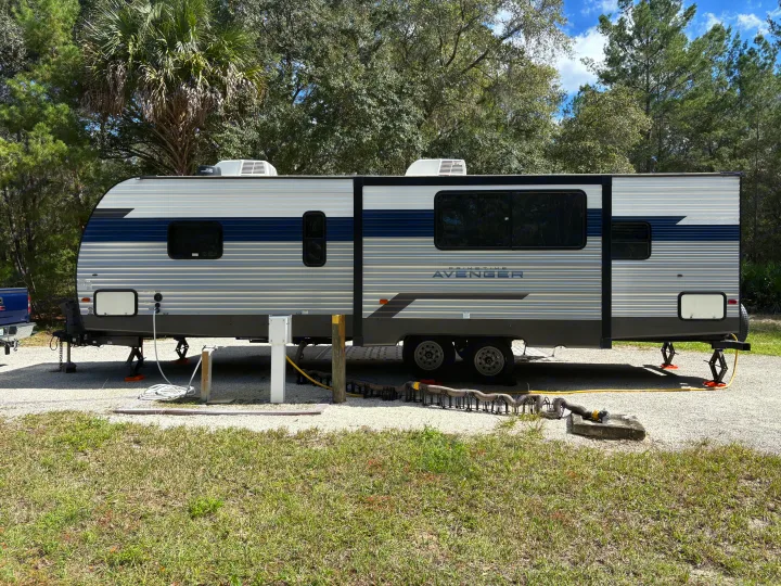 This RV rental, a PrimeTime Avenger travel trailer, is set up with hookups at a sunny campground site.. Avenger Avenger Trailer 2022