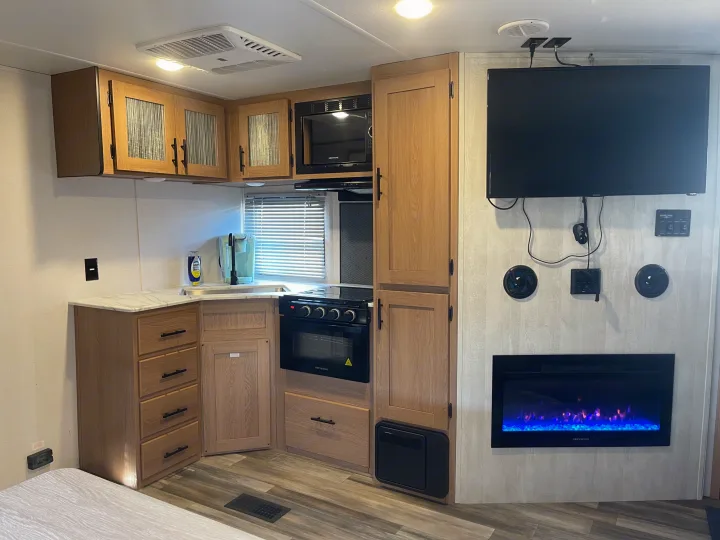 Modern RV rental kitchen with microwave, oven, sink, ample cabinets, plus wall-mounted TV and cozy electric fireplace.. Avenger Avenger Trailer 2022