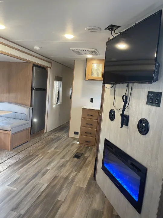 RV rental interior featuring wood-look flooring, a dinette, fridge, wall-mounted TV, and electric fireplace.. Avenger Avenger Trailer 2022