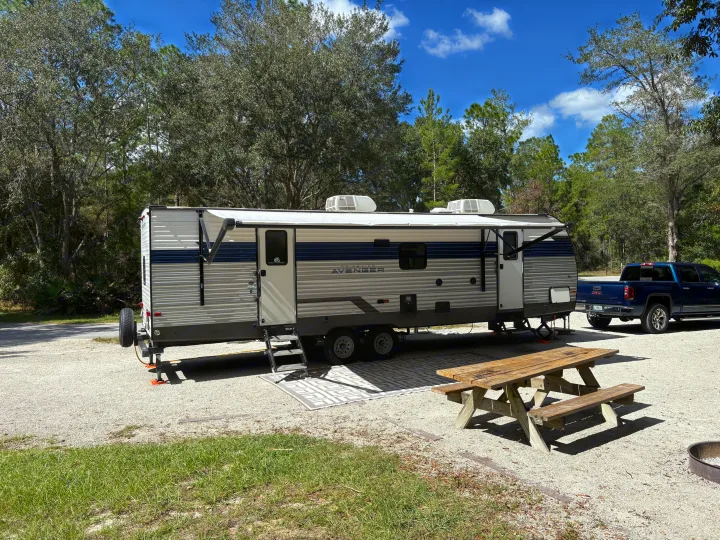 RV rental travel trailer at a sunny campsite with picnic table, fire pit, and truck. Perfect for your outdoor adventure!. Avenger Avenger Trailer 2022