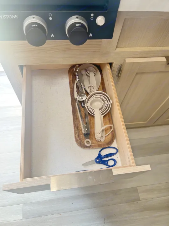 Organized RV rental kitchen drawer with measuring cups, spoons, tongs, and scissors under a stovetop.. Forest River Salem FSX 2023