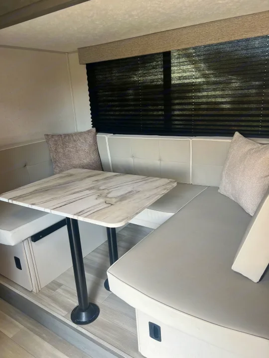 Cozy rv rental dinette with U-shaped bench seating, light gray cushions, white marble-look table, and dark window blinds.. Forest River Salem FSX 2023