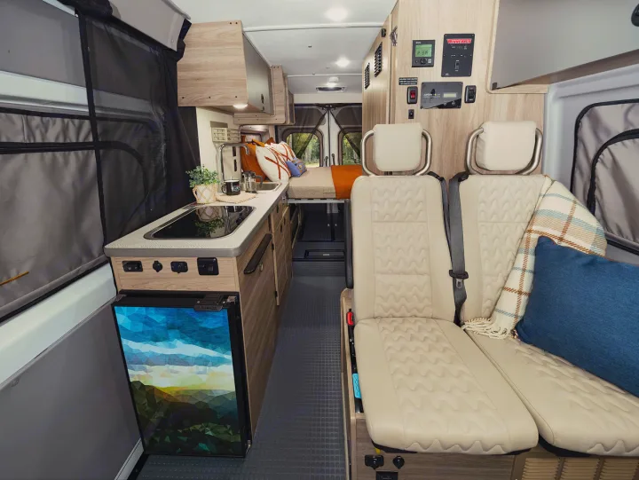 Cozy rv rental interior: kitchenette with fridge, comfy seating, and bed create a welcoming camper van travel space.. Winnebago Solis 2025