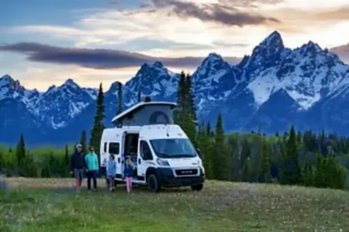 A family enjoys their RV rental parked in a field, with grand snow-capped mountains towering behind.. Winnebago Solis 2025