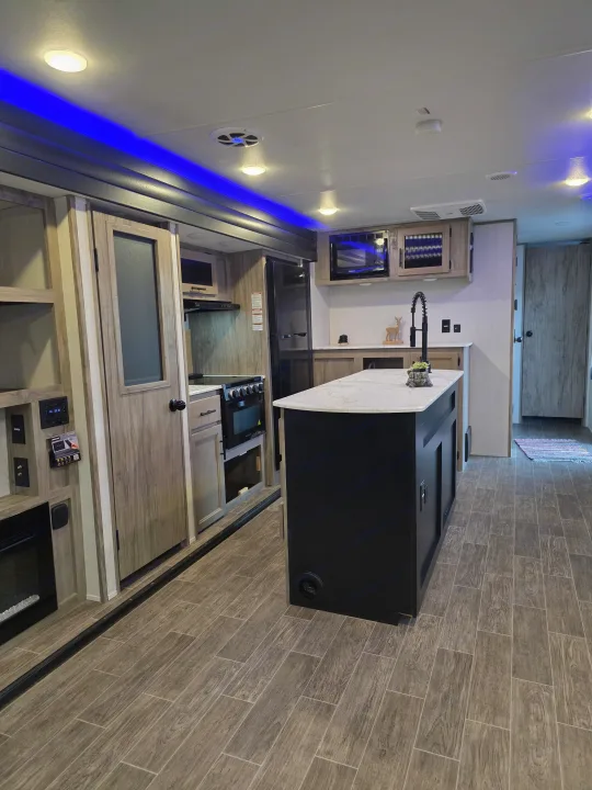 Spacious, modern RV rental interior with kitchen island, appliances, wood-look floor, and blue accent lighting.. Forest River Cherokee Alpha Wolf 2022