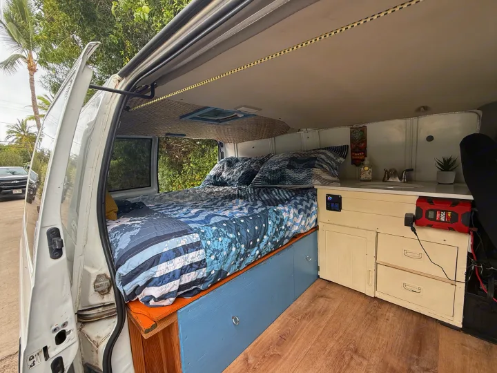 This cozy RV rental features a custom campervan interior with a bed, kitchenette, and wood floor, perfect for mobile living.. Chevrolet Other 2005
