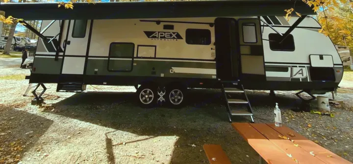 Autumn RV rental at a scenic campsite. Golden leaves, blue sky, and a person on the roof doing maintenance.. Coachmen Other 2022