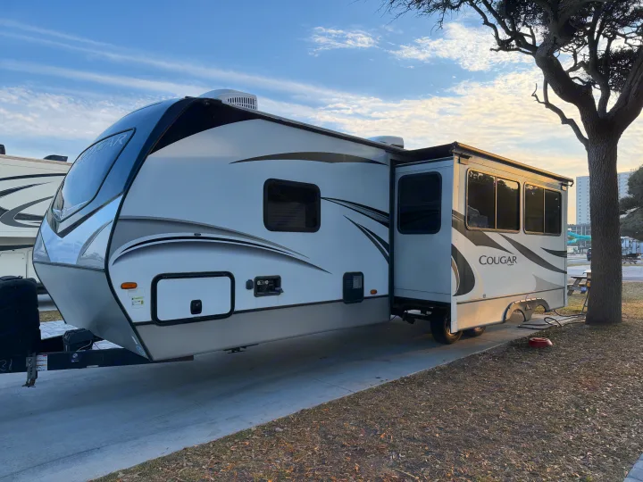 Bright, modern Cougar travel trailer RV rental with slide-out extended, parked on a concrete pad at a sunny campsite.. Keystone Cougar Half-Ton 2020
