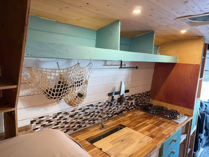 Compact RV rental kitchen with wood ceiling, turquoise shelves, mosaic backsplash, sink, and gas stove for adventure travel.. Ford Transit 2021